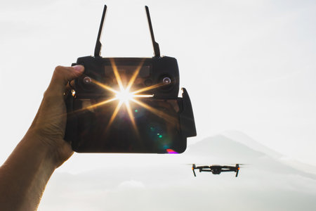 Close up drone remote control in hand. Wireless drone control. Silhouette and sun at sunrise.の写真素材