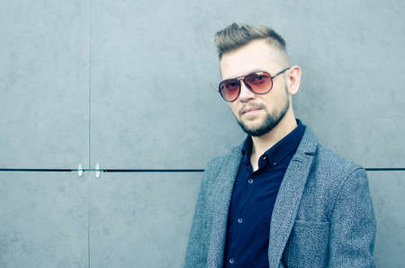 a man with a beard in sunglasses and a jacket against a gray wallの写真素材
