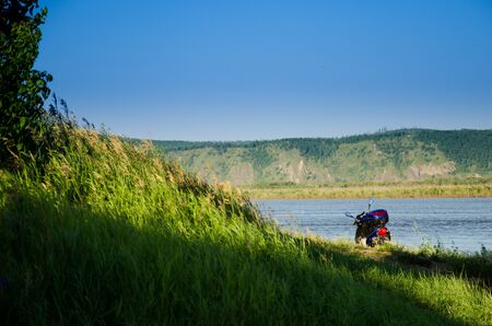 motor scooter near a hill with green grass near the river on a sunny summer dayの写真素材