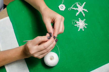 woman knits a white snowflake out of a thread on a table covered with green decorative napkinの写真素材