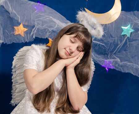girl in angel costume sleeps on a background of dark blue sky with foil starsの写真素材