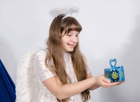smiling girl in angel costume holds a gift in palmsの写真素材