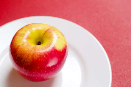 ripe red-yellow apple on a white plate against the red backgroundの写真素材