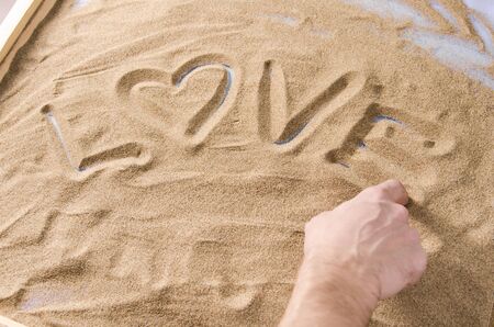 a man draws by his  finger on the sand word love with symbol of heart