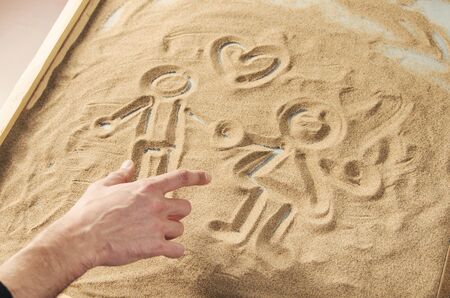 a man draws by his  finger on the sand figures of man and woman with symbol of heart above themの写真素材