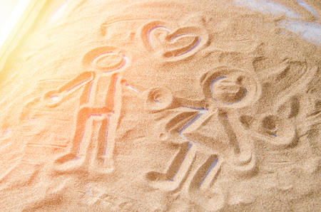 drawn on the sand figures of a man and a woman with a symbol of the heart above themの写真素材