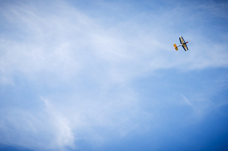 Small hand-crafted wooden plane against a blue sky with white cloudsの写真素材