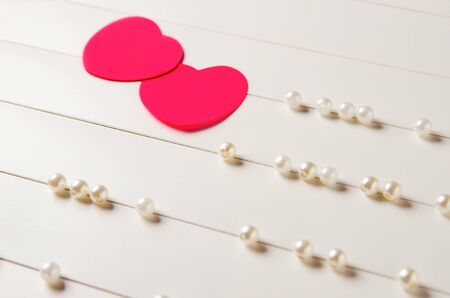 two red paper hearts on a light striped background with pearl beadsの写真素材