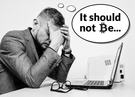a sad man in a suit withhis hands covering his face behind his desk with a laptop thinks it should not be. The symbol bitcoin is used. The concept of the collapse of bitcoin or the loss of savings of crypto currency.の写真素材