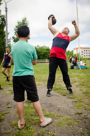 KOMSOMOLSK-ON-AMUR, RUSSIA, AUGUST 1, 2015. Public open Railroader's day. boy is looking at man raises a weight in an amateur competitionのeditorial素材