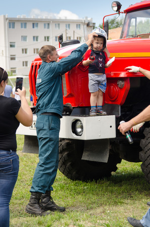 Komsomolsk-on-Amur, Russia - August 8, 2016. Public open Railroader's day. firefighter puts on a fire helmet on the boy who is standing on the step of the fire engineのeditorial素材