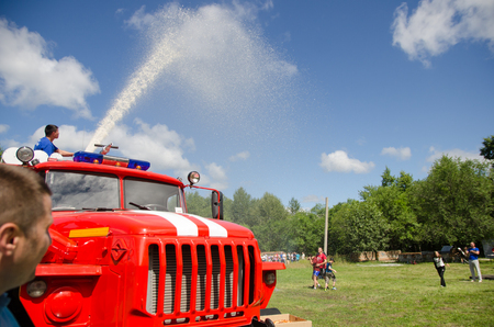 Komsomolsk-on-Amur, Russia - August 8, 2016. Public open Railroader's day. fireman on fire truck pours water from fire cannon on joyful participants in amateur competitionsのeditorial素材