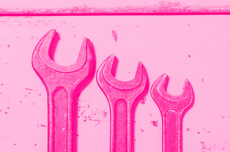several wrenches on the background of metal painted plates. pink toned. concept of feminism.