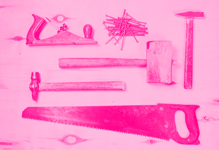 set of tools for working on a timber - saw, plane, hammers, mallet, nails - lay on a sheet of plywood. flat view. pink toned. concept of feminism.の写真素材