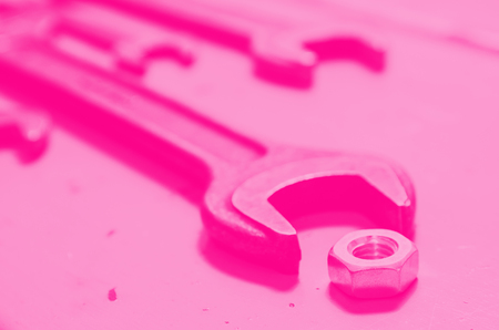 several wrenches and screw-nut on the painted metal background. pink toned. concept of feminism.の写真素材