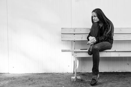pensive beautiful girl with long hair sitting on bench.の写真素材