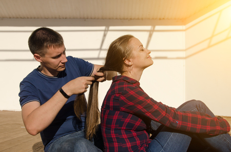 guy with a short haircut braids a girl with long dark hair and a plaid shirt.の写真素材
