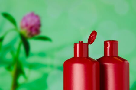 pair of red plastic bottles from under a cosmetic product on a green background with an blurred image of clover.の写真素材
