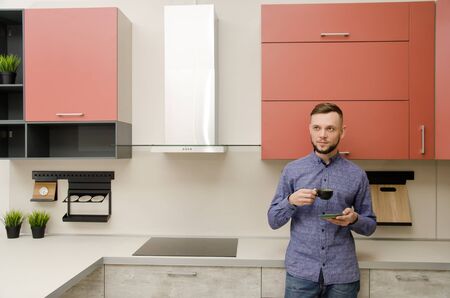 Attractive bearded man standing drinks coffee in a modern kitchen.の写真素材