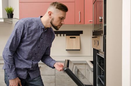 attractive bearded man peeks into an oven in a modern kitchen.