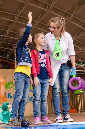 Komsomolsk-on-Amur, RUSSIA - AUGUST 27, 2018. Showing physical and chemical experiments for children. A woman with a special air gun for school experiments and two volunteer schoolchilds. vertical.のeditorial素材