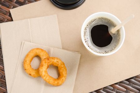 coffee in a paper cup next to onion rings on a paper napkin. Unhealthy fast food.の写真素材