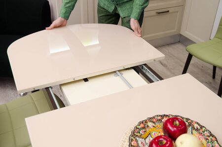 man shifts a sliding glossy dining table on which stands a plate with artificial fruit.の写真素材