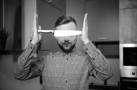 strange bearded man holds a knife between two hands in front of his face.の写真素材