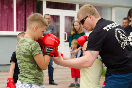 Komsomolsk-on-Amur, RUSSIA - JULY 21, 2018. Kickboxing coach shows the boy how to make punch in sparring. Training outdoor in summerのeditorial素材