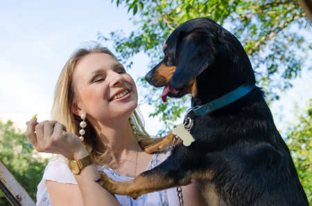 Beautiful blonde girl in a light dress is playing with a cute small dog.