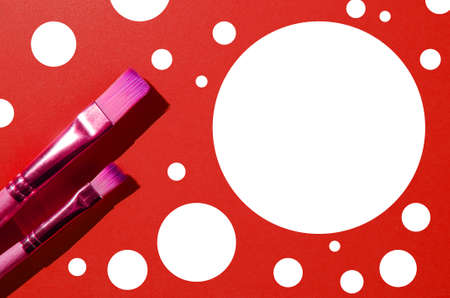 Two paint brushes of different sizes next to white circle on an red background. Place for your text.の写真素材