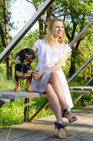 A beautiful blonde young woman with dog is sitting on a park bench. Vertical view.の写真素材
