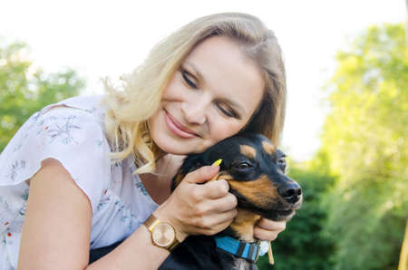 A beautiful blonde young woman in a light dress with tenderness hugs her cute dog.の写真素材
