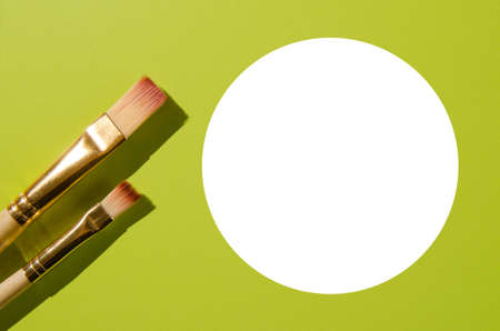 Two paint brushes of different sizes next to white circle on an olive background. Place for your text.の写真素材