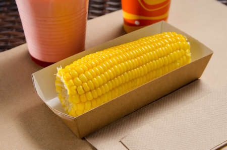 an ear of boiled corn in an eco-friendly cardboard box next to a milkshake and popcorn.の写真素材