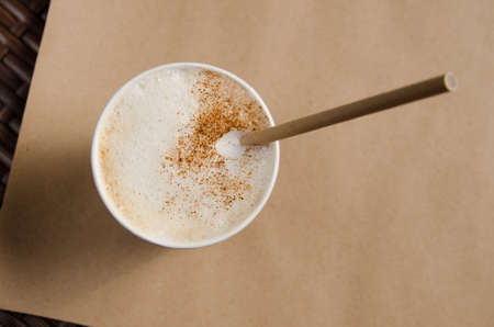 cappuccino coffee with vanilla crumbs in a brown disposable paper cup with a straw.の写真素材