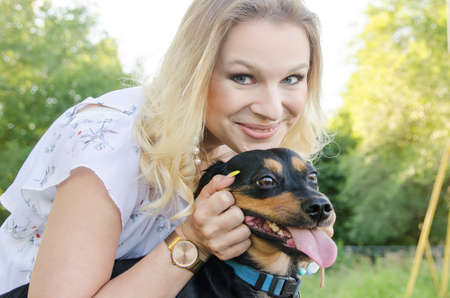 A beautiful blonde young woman in a light dress with tenderness hugs her cute dog.の写真素材