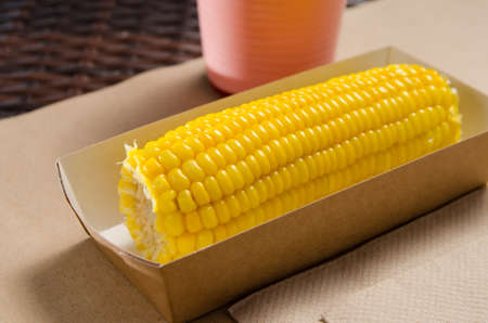 an ear of boiled corn in an eco-friendly cardboard box next to a milkshake.の写真素材