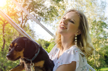 A beautiful blonde young woman in a light dress with tenderness hugs her cute dog.の写真素材