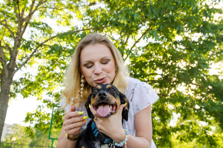 A beautiful smiling blonde young woman in a light dress with tenderness hugs her cute dog.の写真素材