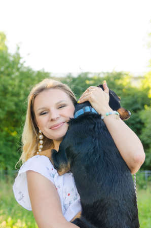 A beautiful smiling blonde young woman in a light dress with tenderness hugs her cute dog. Vertical view.の写真素材