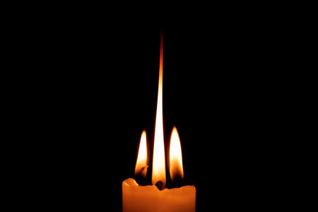 Yellow candle light burn against black background, lit candle with quite flameの写真素材