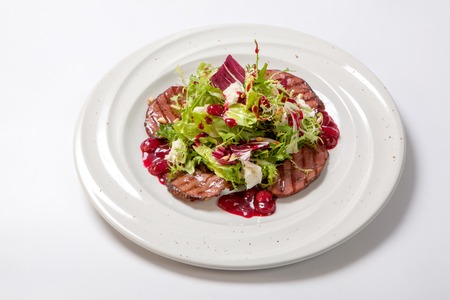 Salad with grilled veal and fresh salad leaves with cherry sauce on a white plateの写真素材