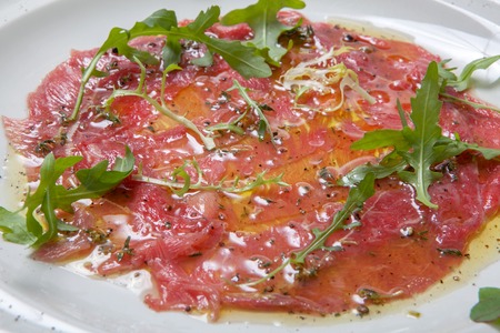 Beef carpaccio with vegetable oil, garnished with fresh arugula and topped with ground black pepper on a round white plateの写真素材