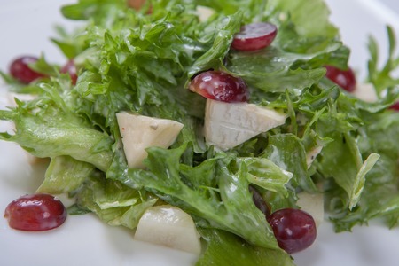Salad with fresh lettuce leaves with slices of melon and grapes, dressed with a sweet sauce on white plateの写真素材