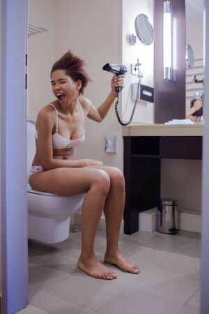 Young beautiful woman dries her hair, using hairdryerの写真素材