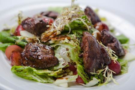 warm salad with chicken liver and grapes on the white plateの写真素材