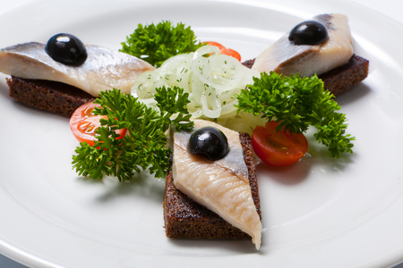 Sliced black bread and herring and fresh onion on a white plateの写真素材