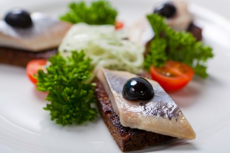 Sliced black bread and herring and fresh onion on a white plateの写真素材