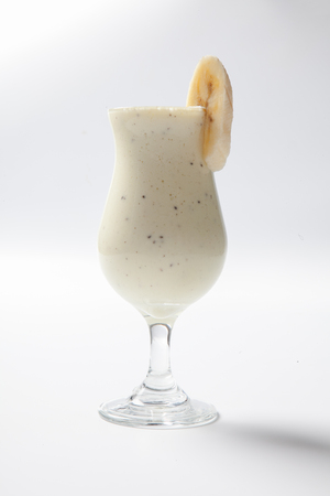 banana milkshake with a piece of banana in a tall glass on white background.の写真素材